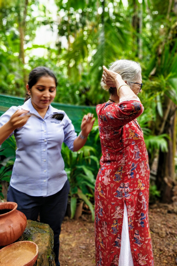 Tourists experiencing the traditional welcome ritual at spice plantation where guide pours water and lavender oil mixture down visitors' backs for a refreshing sensation