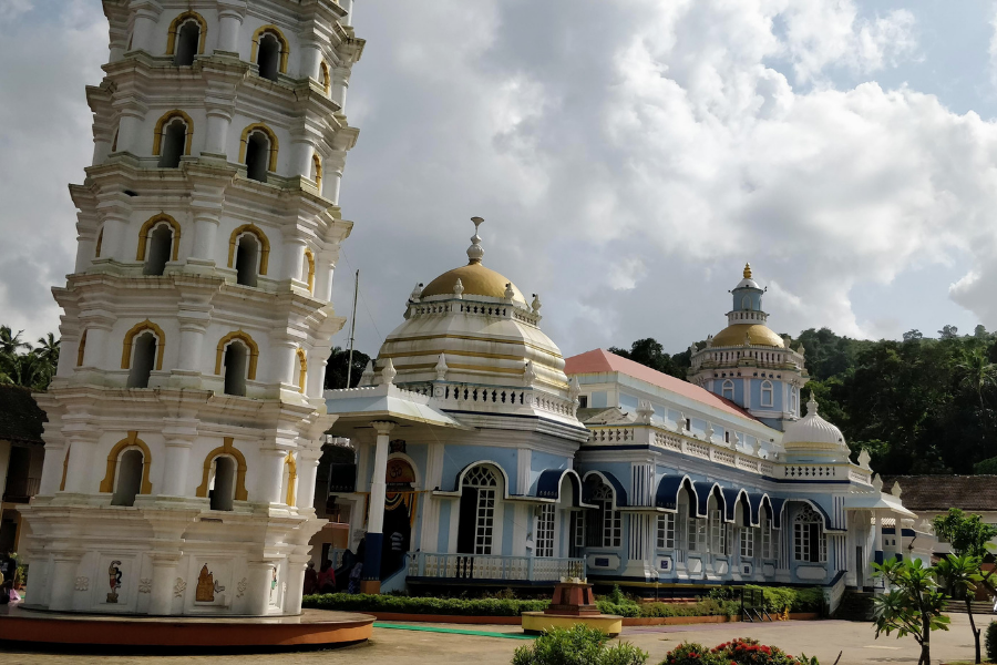 Impressive exterior of Shri Mangeshi Temple in Priol showing the distinctive multi-tiered golden tower (deepstambha), ornate architecture, and illuminated facade