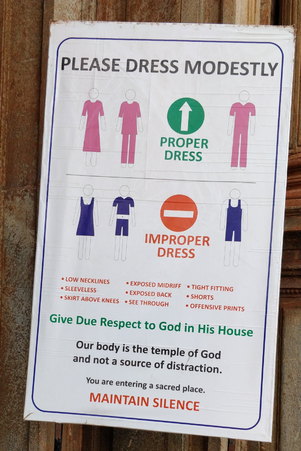Sign board at the entrance of Se Cathedral displaying dress code guidelines for visitors including restrictions on sleeveless tops, shorts, and revealing clothing